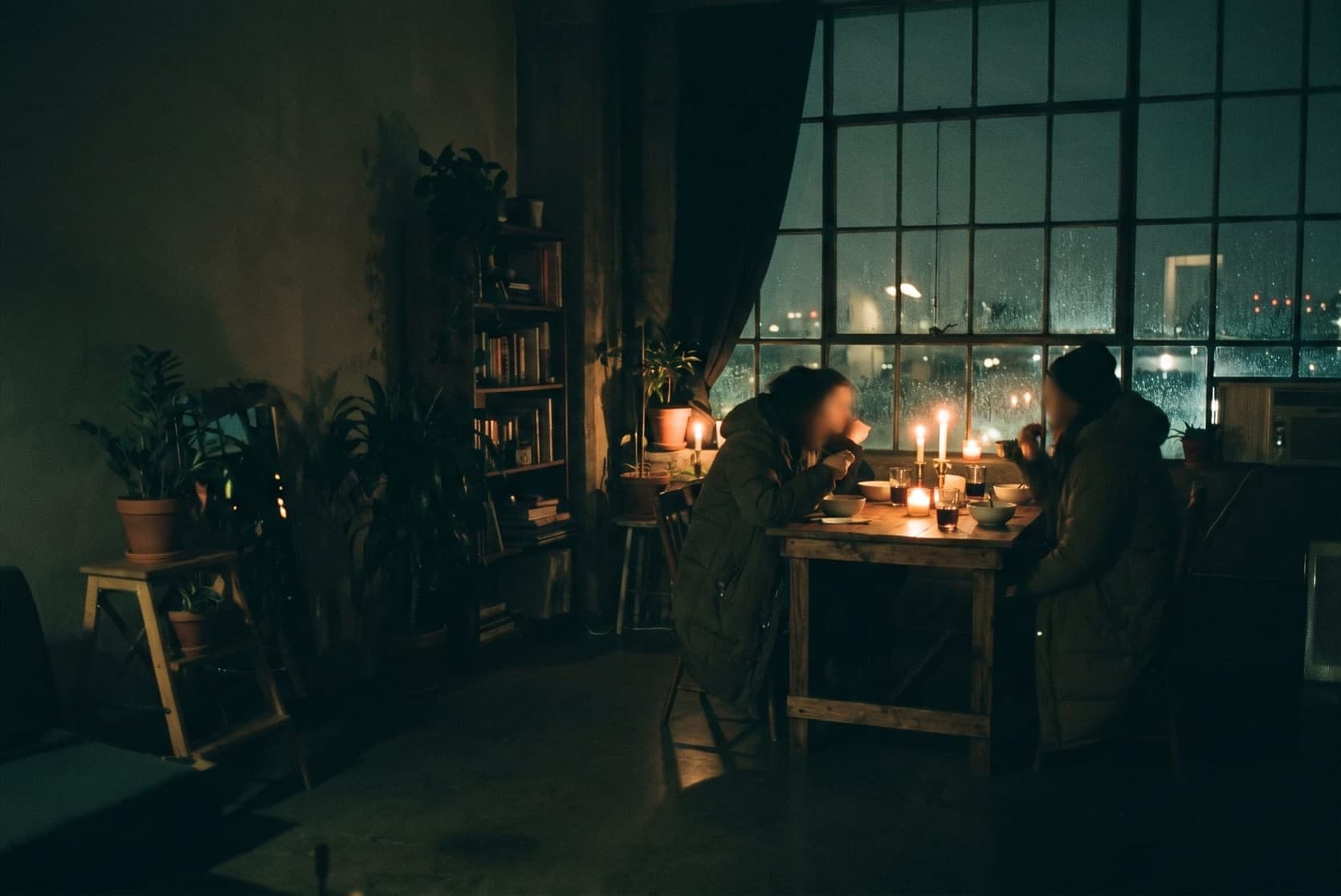 Two people sharing a quiet dinner by a rain-streaked window at night.